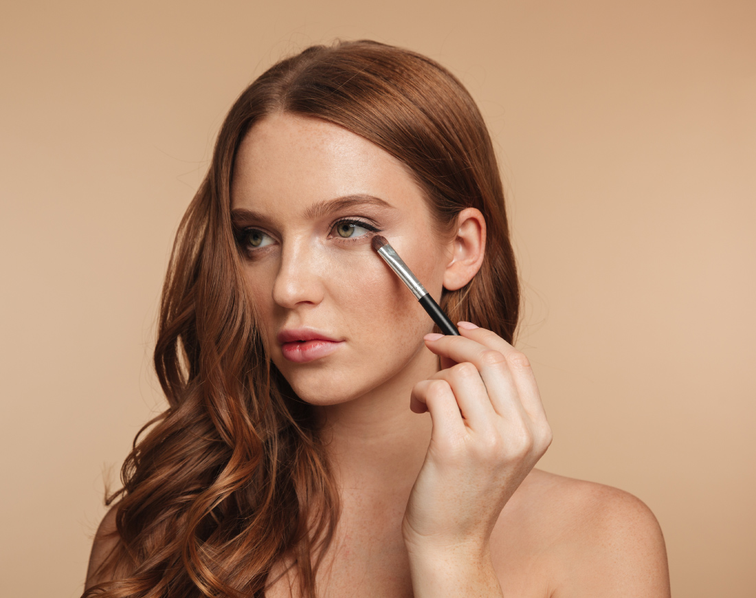 Mujer pelirroja maquillando sus ojos con una brocha